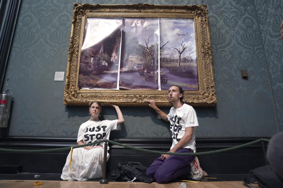 Protesters glue their hands to the frame of John Constable's The Hay Wain after first having covered the painting with their own picture, inside the National Gallery, London, Monday July 4, 2022. Police say two climate change protesters have been arrested after they glued themselves to the frame of a famous John Constable painting hanging in Britain’s National Gallery. The two, from the protest group “Just Stop Oil,” stepped over a rope barrier and covered “The Hay Wain” on Monday with large sheets of paper depicting “an apocalyptic vision of the future” of the landscape. (Kirsty O'Connor/PA via AP)