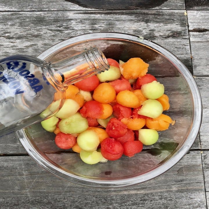 Pouring vodka into a bowl of melon balls.