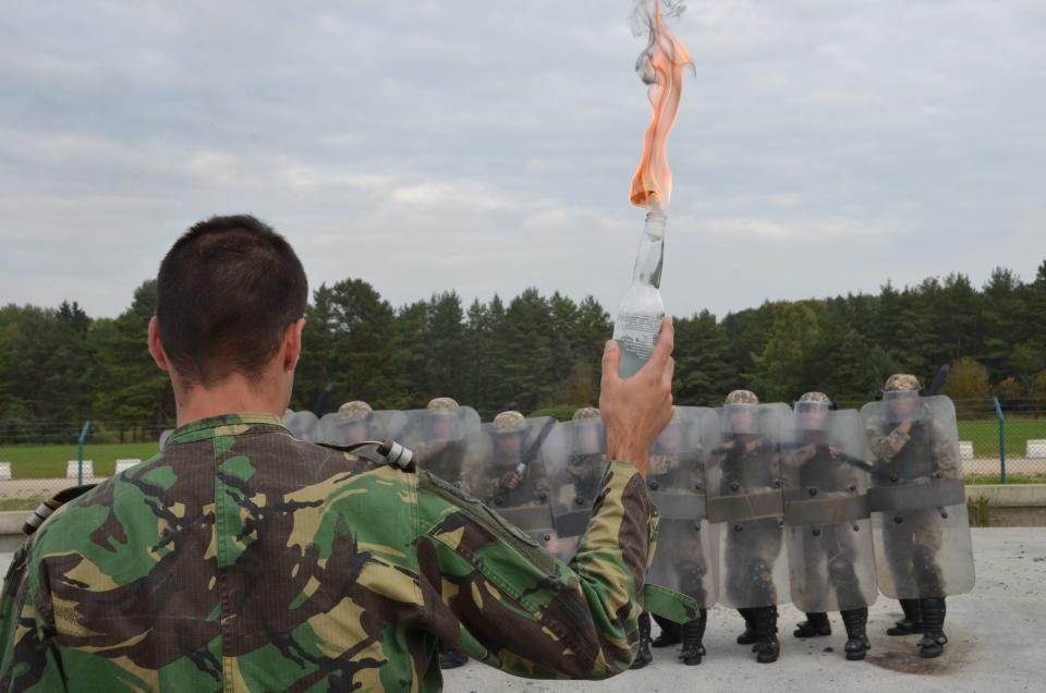 A photo of a man in army fatigues holding a lit Molotov cocktail in his hand.