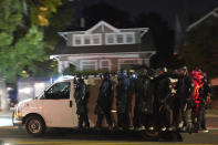 Portland police hang off the side of a riot van while searching for protesters in the Laurelhurst neighborhood after dispersing a crowd of about 200 people from in front of the Multnomah County Sheriff's Office early in the morning on Saturday Aug. 8, 2020 in Portland, Ore. (AP Photo/Nathan Howard)