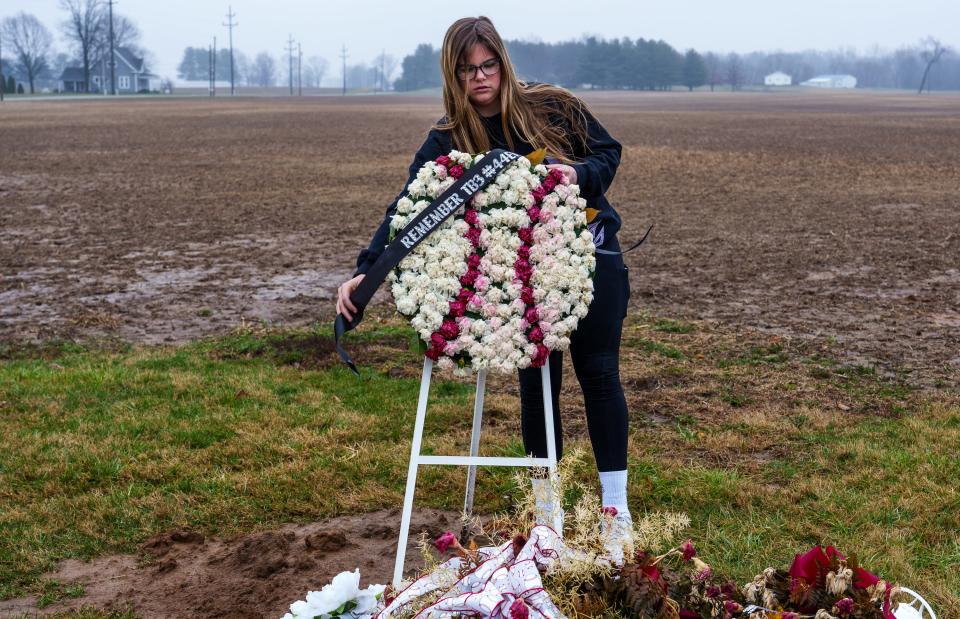 After a windy and wet morning, Lila Badger attaches a ribbon Thursday, March 23, 2023, to a floral baseball marking the gravesite of her cousin, Terry Badger III, who died by suicide weeks prior. The two grew up close, spending many days together.