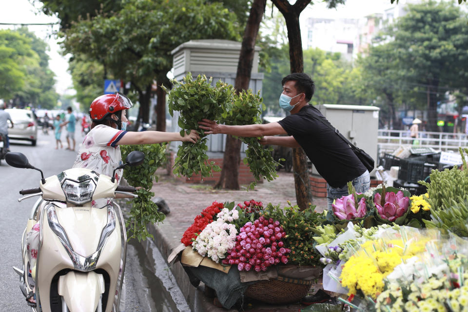 A seller hands flowers to a customer, both wearing face masks, in Hanoi, Vietnam, Monday, Aug. 3, 2020. Vietnam has tightened travel and social restrictions after the country's death toll of COVID-19 to six. (AP Photo/Hau Dinh)