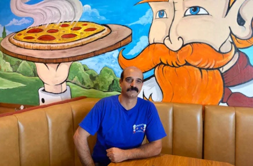 Magdy Faltaous, owner of 2 Boys Pizza and Grill, sits in a booth under a custom mural at the restaurant's former Augusta location. The restaurant moved to its new Evans location in March 2024.