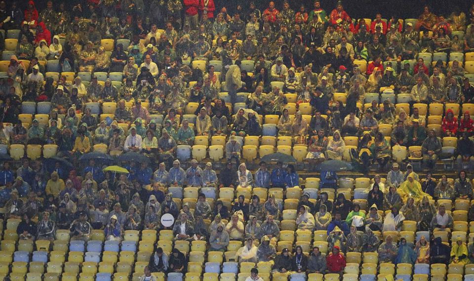 <p>Spectators in rain ponchos and holding umbrellas sit in the stands. REUTERS/Yves Herman </p>