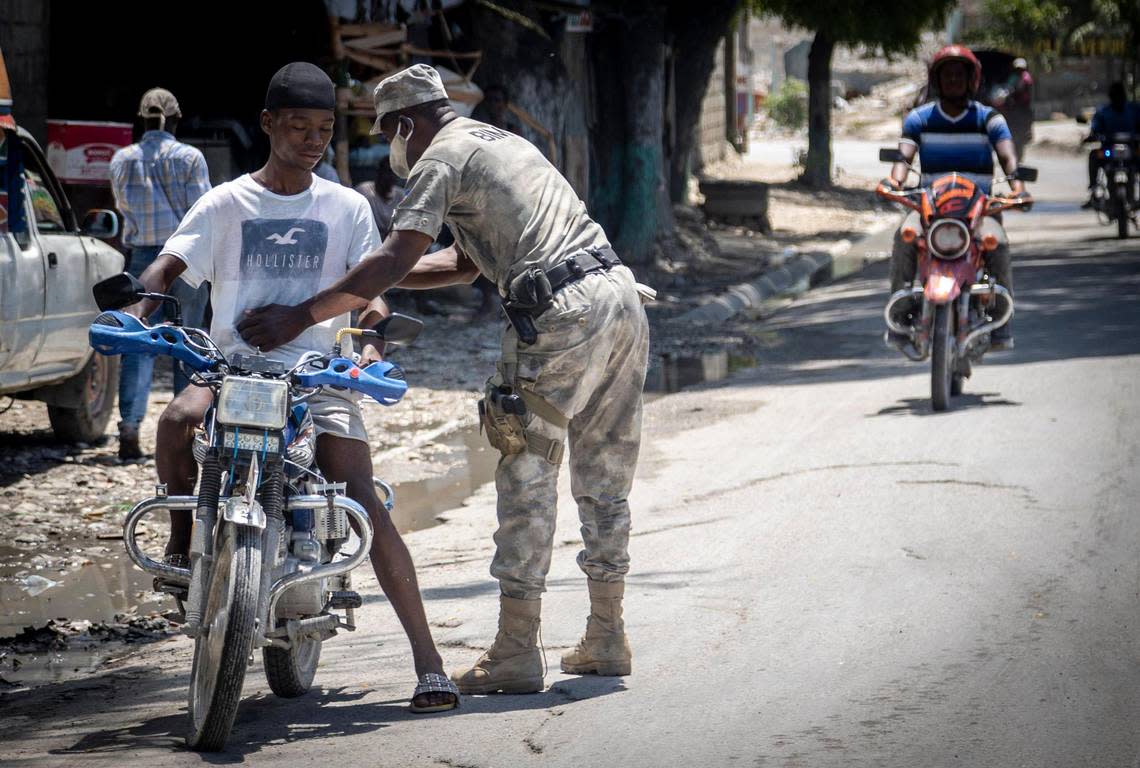 A Haitian policeman frisks a motorcyclist at a checkpoint on June 23, 2022, in Butte-Boyer 75, where a deadly gang war erupted in late April. Police launched a military-style incursion to take back the key intersection.