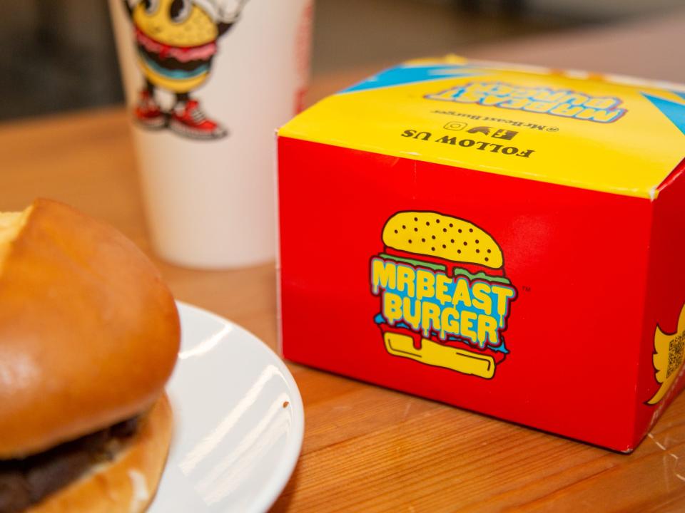 A burger on a plate next to a cup and packaging