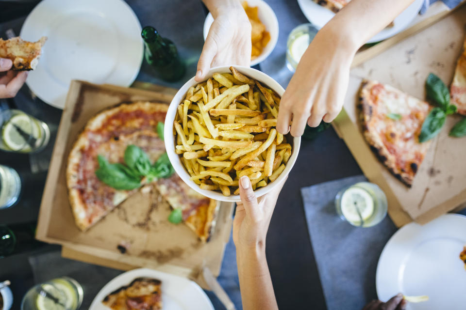 Person reaching for fries with trans fats and pizza in the background.