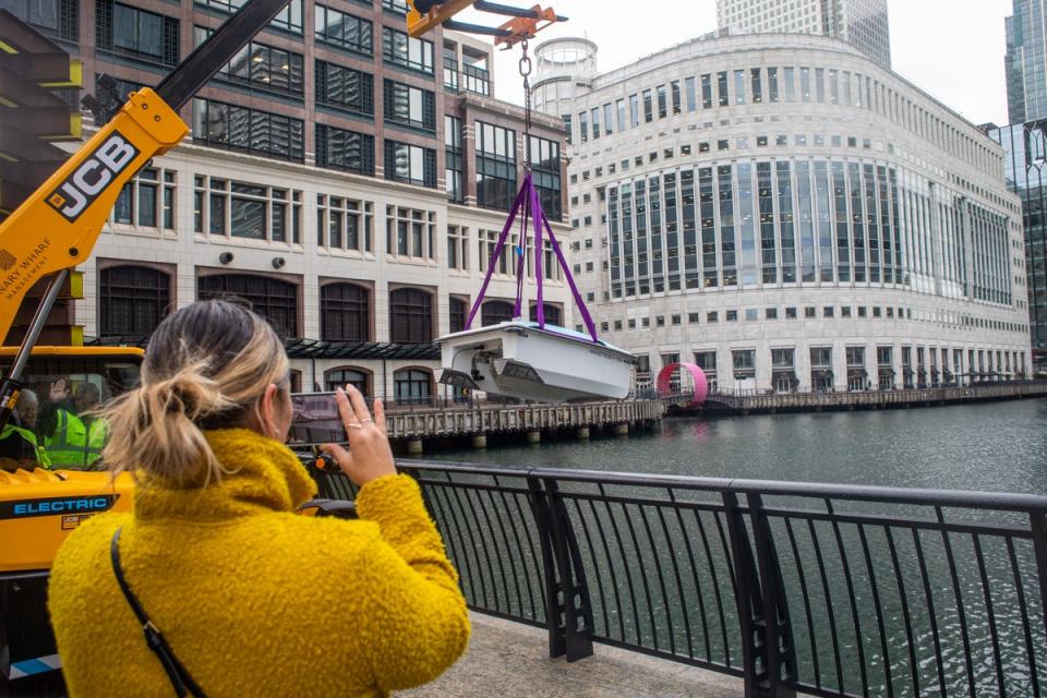 A woman takes a picture as the WasteShark is lowered into the Middle Dock of Canary Wharf ahead of Global Recycling Day (Aqua Libra)