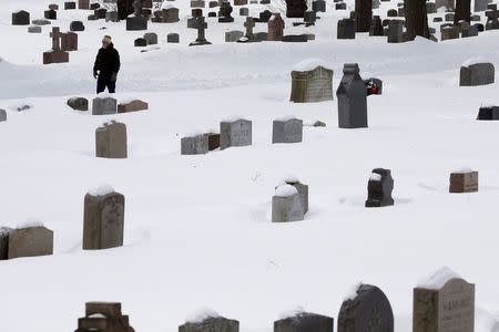 A man walks among snow-covered tombstones at St. Paul's Cemetery in Arlington, Massachusetts, February 18, 2015, following a series of winter snowstorms in the Boston area. REUTERS/Brian Snyder