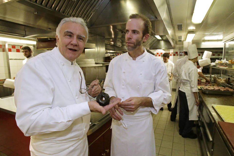 This Oct. 9, 2012 photo shows Alain Ducasse holding an apple as American Chef Dan Barber stands next to him in the kitchen of the Plaza Athenee in Paris. He fires up the succulent pork over gnarled, carbonated pig bones, grows sweet greens in a soil mixed with pumice that's left over by the hazelnut oil industry and he's creating a new kind of wheat, named after himself _ Dan Barber. (AP Photo/Michel Euler)