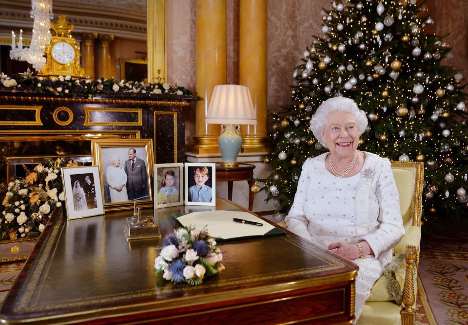 <p>Queen Elizabeth's smile shines brighter then the Christmas tree behind her in this festive shot. She'd just finished recording her annual holiday message at her desk, filled with family pictures, in the 1844 Room at Buckingham Palace.</p>