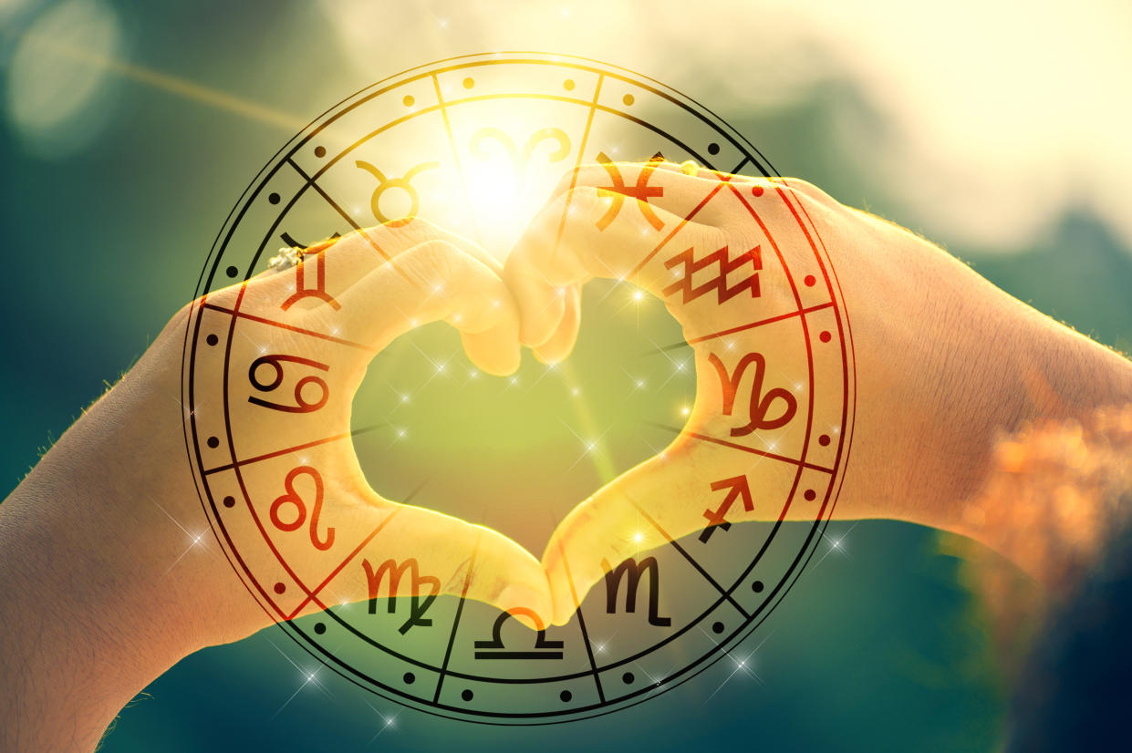 Sunlight passing through two hands making a heart shape behind astrological symbols. (Getty Images)