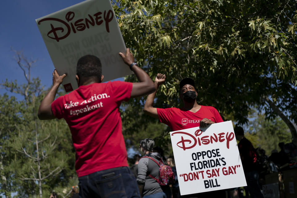 Two LGBTQ supporters hold signs to protest Disney’s stance on LGBTQ issues. - Credit: AP Photo/Jae C. Hong