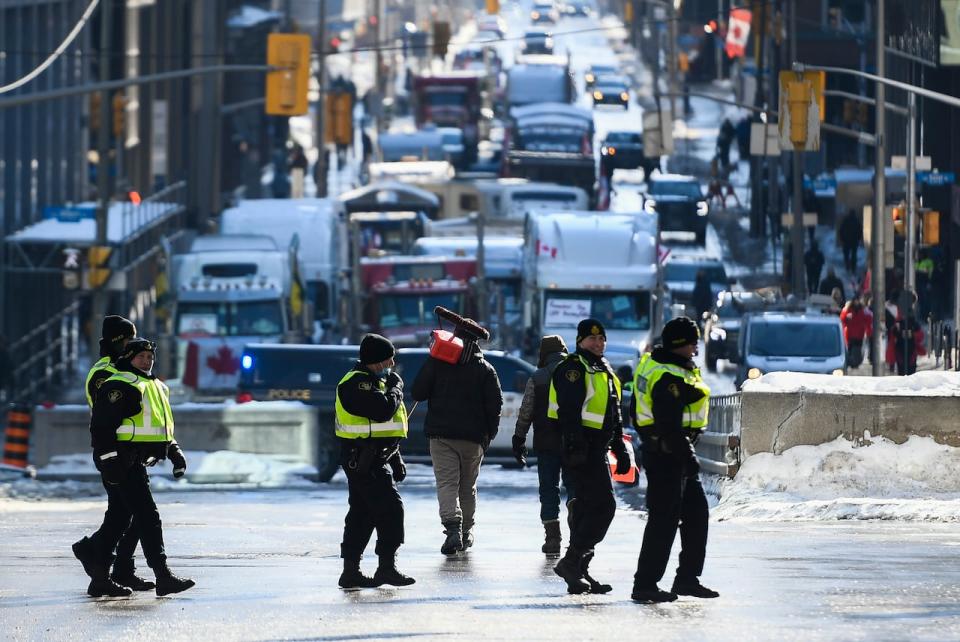 A protester carrying an empty fuel container on a broom handle walks on Metcalfe Street past Ontario Provincial Police officers Feb. 7, 2022 during the ongoing protest against COVIFD-19 rules in Ottawa.