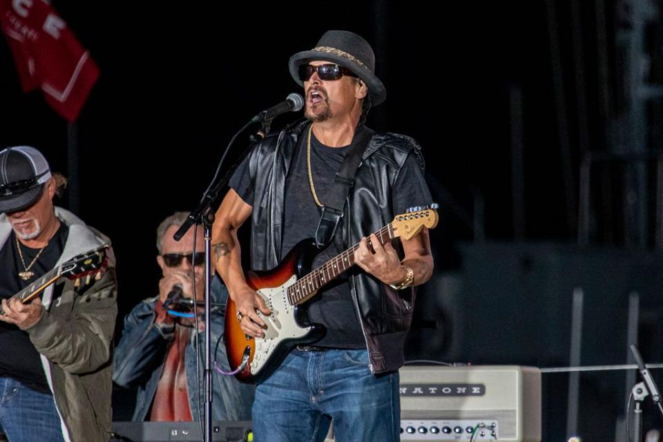 kid rock playing guitar and singing into a microphone on a stage