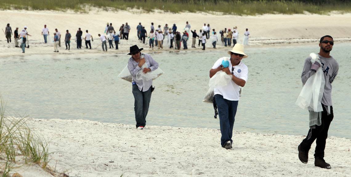 Workers carry bags of seagrass mixed with tar balls from a beach at St Andrews State Park in Panama City, June 21st, 2010. The tar balls are suspected to be from the BP oils spill in the Gulf of Mexico. About eighty workers comb the beach to remove the tar balls that have been moving slowly eastward into waters off Florida.