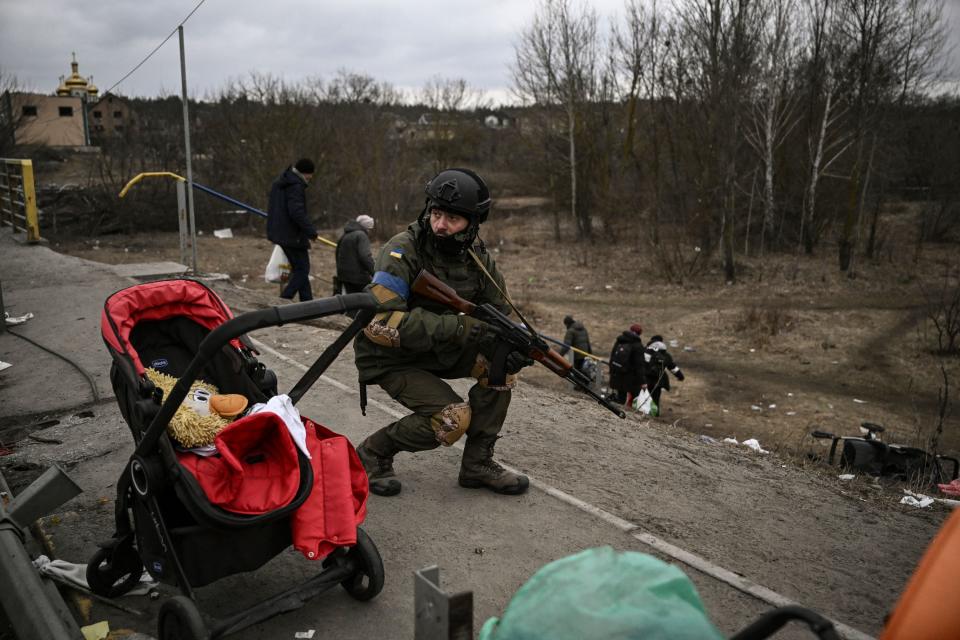 TOPSHOT - An Ukrainian serviceman takes cover as people evacuate  the city of Irpin on March 13, 2022. Russian forces advance ever closer to the capital from the north, west and northeast. Russian strikes also destroy an airport in the town of Vasylkiv, south of Kyiv. A US journalist was shot dead and another wounded in Irpin, a frontline northwest suburb of Kyiv, medics and witnesses told AFP. / AFP / Aris Messinis