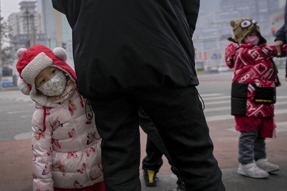 Children wearing face masks to help protect from the coronavirus stand with relatives waiting to cross a traffic intersection in the Central Business District of Beijing, Monday, Jan. 24, 2022. A fresh outbreak in Beijing has prompted authorities to test millions and impose new measures two weeks ahead of the opening of the Winter Olympics, even as Chinese officials on Monday lifted a monthlong lockdown on the northern city of Xi'an and its 13 million residents. (AP Photo/Andy Wong)