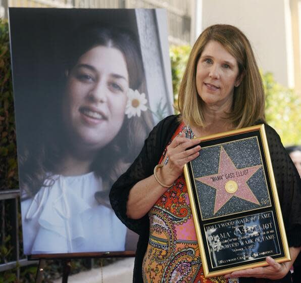 A woman holds a framed Hollywood Walk of Fame replica star in front of a large photo of late singer 'Mama' Cass Elliot