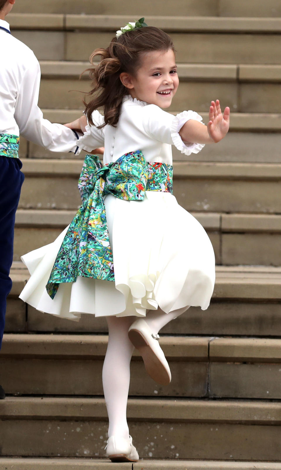 A bridesmaid gives a wave to the crowds.&nbsp;