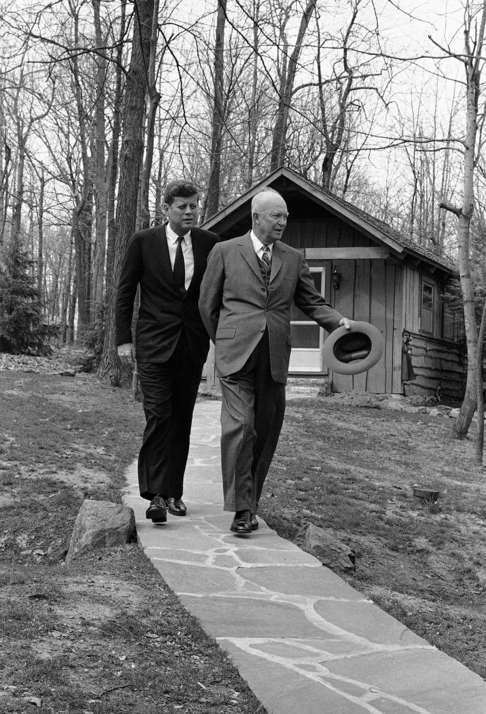 President John Kennedy and former President Dwight Eisenhower walk along a flagstone path at Camp David atop a mountain near Thurmont, Md. on April 22, 1961 after they flew here to discuss the Cuban crisis. In background is one of the lodges at the camp.