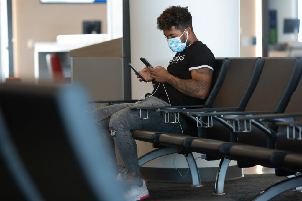 An airline passenger waiting for his flight looks at his phone while wearing a protective face mask.