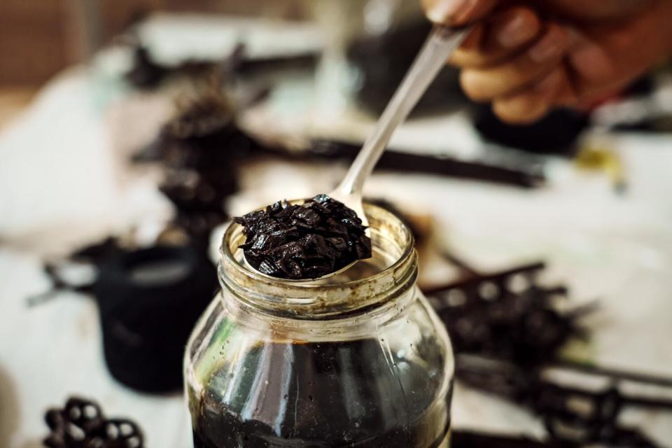 A hands holds a spoonful of a black substance from a glass jar