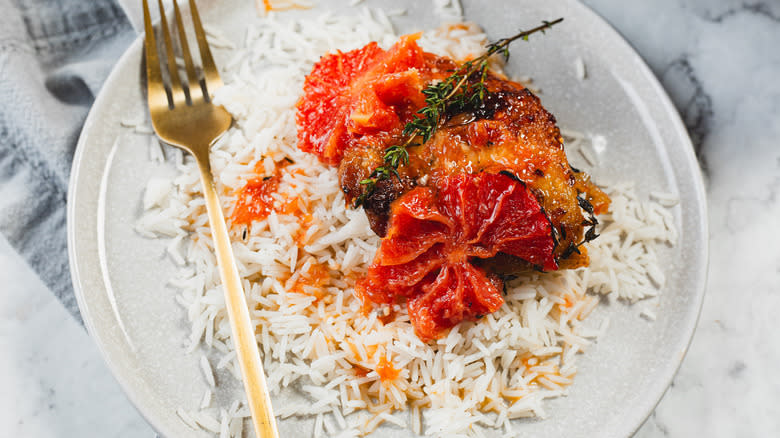 A plate of rice, chicken, and grapefruit