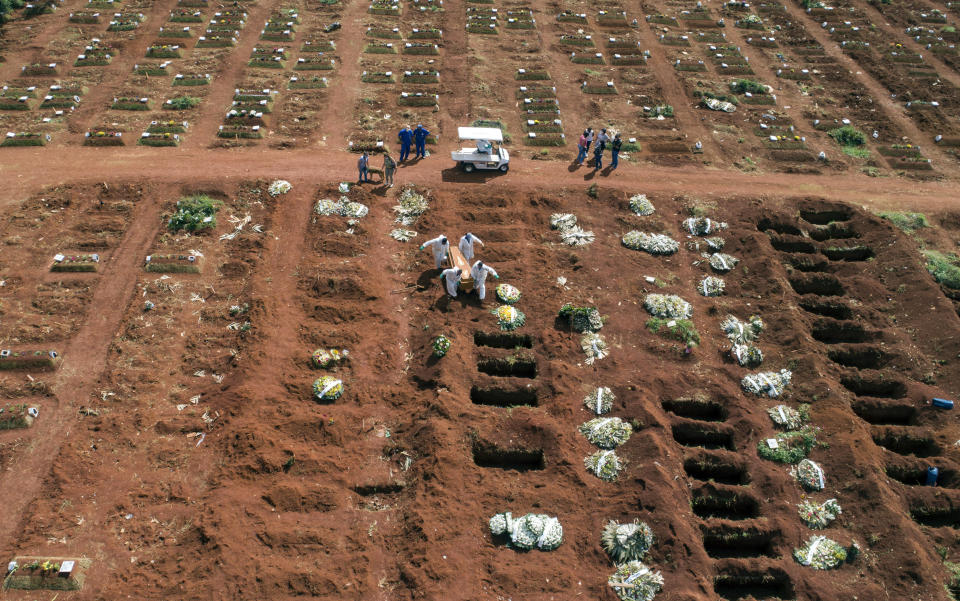 Cemetery workers wearing protective gear carry the coffin of a person who died from complications related to COVID-19 to a gravesite at the Vila Formosa cemetery in Sao Paulo, Brazil, Wednesday, April 7, 2021. The city of Sao Paulo started on Wednesday the digging of 600 additional graves every day in its municipal cemeteries. (AP Photo/Andre Penner)