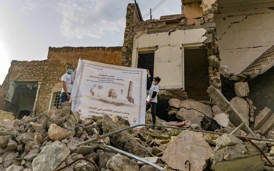 Youths unfurl a poster welcoming Pope Francis next to the ruins of the Syriac Catholic Church of the Immaculate Conception (al-Tahira) in Mosul - ZAID AL-OBEIDI /AFP