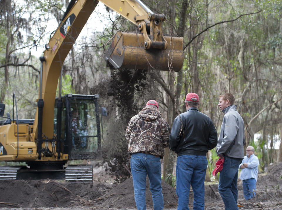 Patrick Sessions, center, and his son Jason, right, watch as Alachua County Sheriffs technicians use a back hoe Thursday, Feb. 2, 2014, in Gainesville, Fla., to dig for evidence in the 1989 disappearance of Tiffany Sessions, a University of Florida student. The sheriffs department announced they have linked the disappearance to Paul Rowles, a serial killer who died in prison last year. (AP Photo/Phil Sandlin)