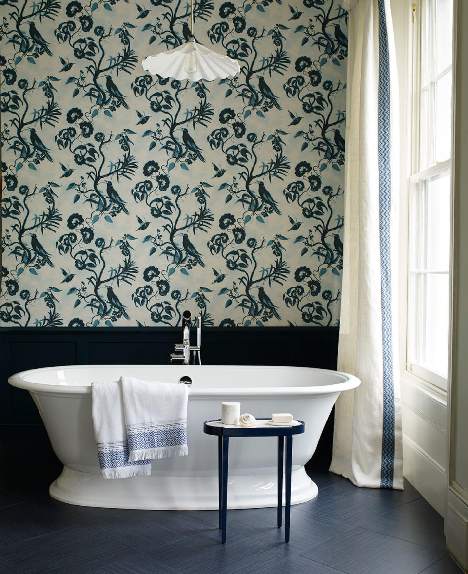 Bathroom with dark blue block color wall panelling and floor with whimsical wallpaper above