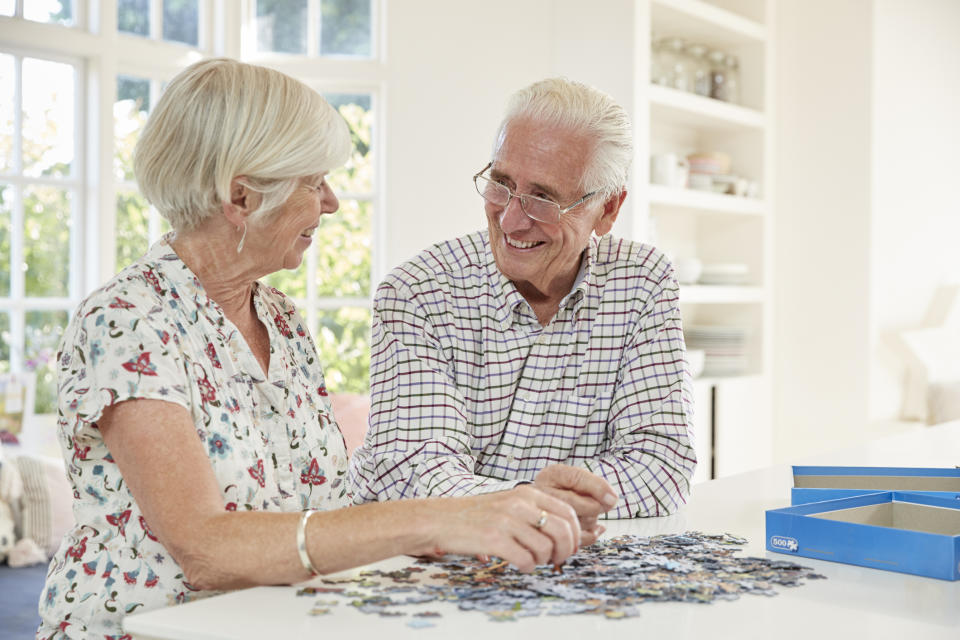 Senior couple seated at a table, doing a puzzle.