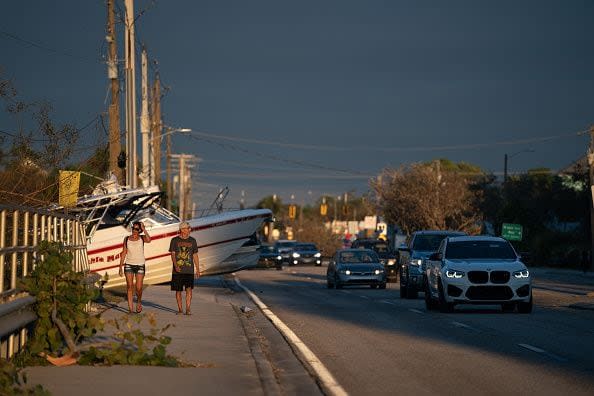 People walk along a sidewalk blocked by boats after Hurricane Ian on September 29, 2022, in Bonita Springs, Florida.