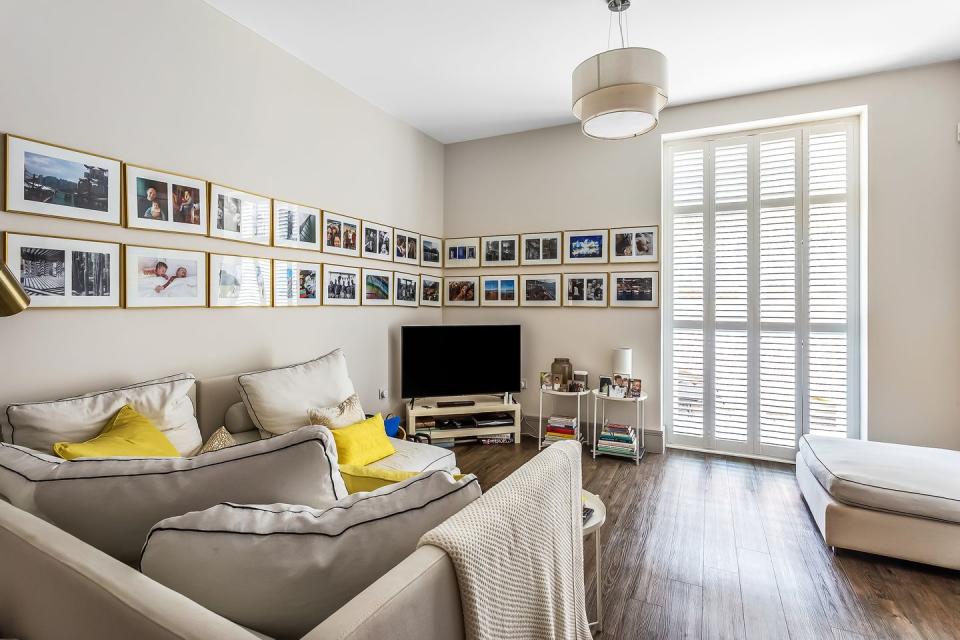 a neutral living room with corner sofa, television and framed photos on the wall