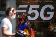 FILE PHOTO: People walk past a 5G data network sign at a mobile phone store in Paris