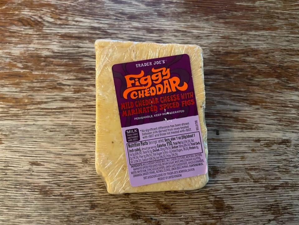 Yellow block of Trader Joe's figgy cheddar with purple label on a wooden cutting board