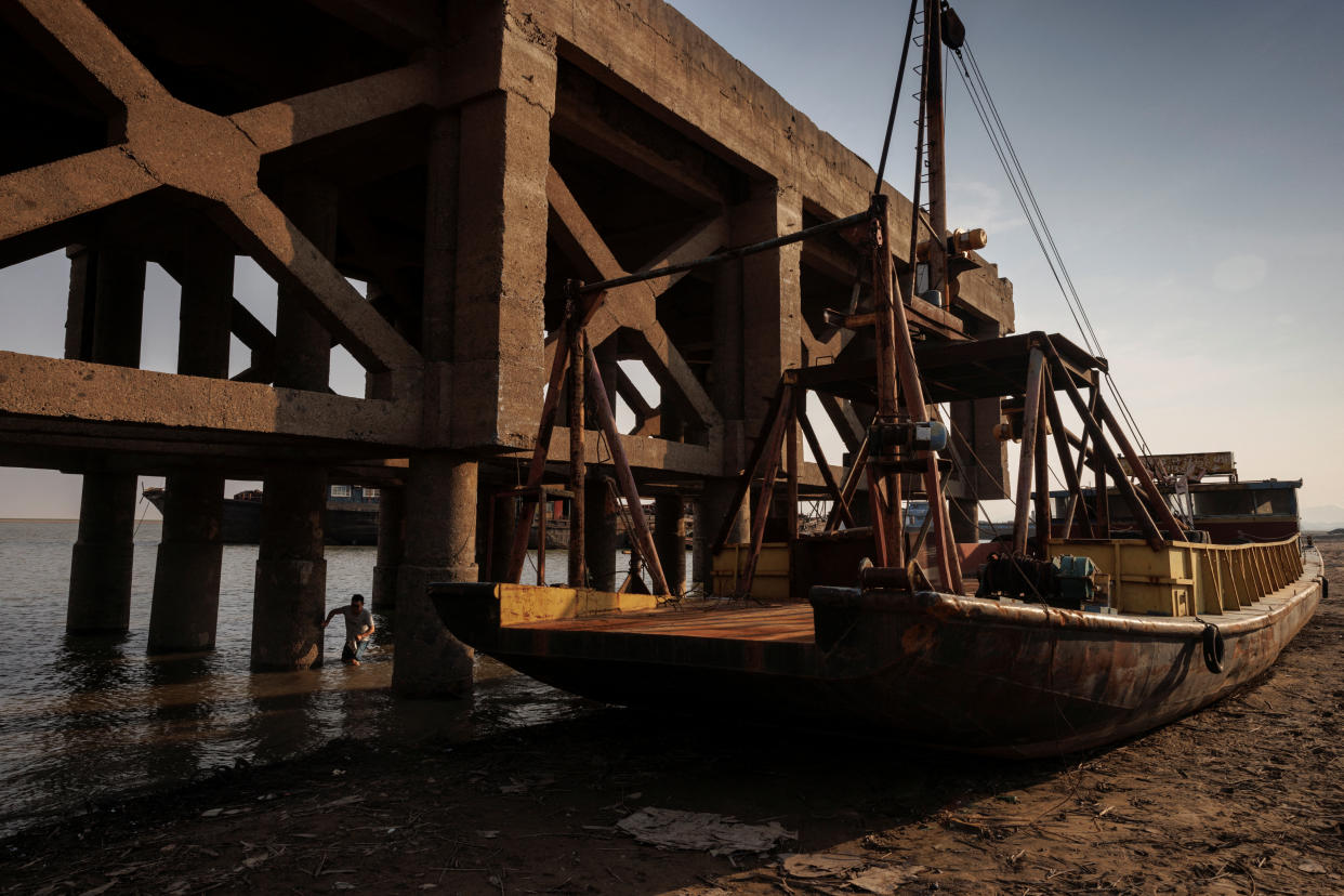 A man collects bait for fishing next to a grounded ship underneath an exposed pier in Poyang Lake which exhibits low water levels because of a regional drought in Lushan, Jiangxi province, China, August 24, 2022.  REUTERS/Thomas Peter