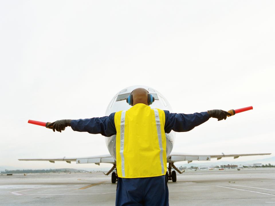 Rear view of an airport ground crew member directing an aircraft