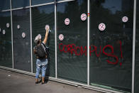 FILE - A protester places a sticker next to a graffiti that reads "corrupt" on the regional ministry of health, during a demonstration in Marseille, southern France, Saturday, Aug. 14, 2021. The run-up to the April election comes in a context of mounting violence targeting elected officials in France, with holders of public officers targeted for their politics and by opponents of COVID-19 vaccinations restrictions. (AP Photo/Daniel Cole, File)