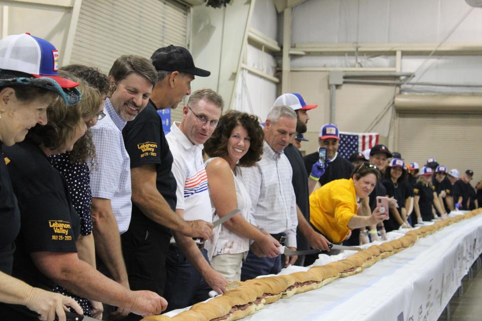 Organizers and local officials gathered together to make the first cuts of the sandwich before serving.