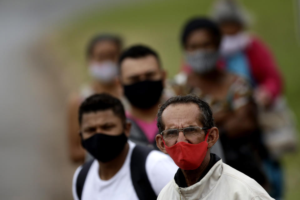 People wear masks against the spread of the new coronavirus, at a bus stop in Valparaiso, Brazil, Wednesday, May 20, 2020. Valparaiso, 40 km. (about 25 miles) from Brasilia, appears in the statistics as one of the cities in the state of Goias with a high incidence of COVID-19. (AP Photo/Eraldo Peres)