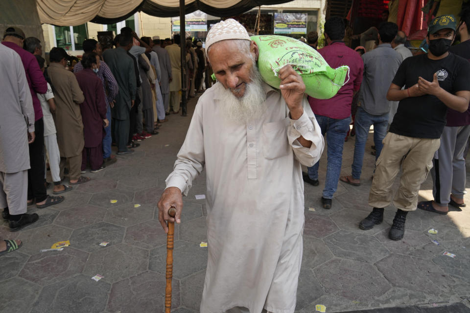 A police officer stands guard while an elderly man leaves after getting a free sack of wheat flour at a distribution point, in Lahore, Pakistan, Thursday, March 30, 2023. Government is providing free flour to deserving and poor families during the Muslim's holy month of Ramadan due to high inflation in the country. (AP Photo/K.M. Chaudary)