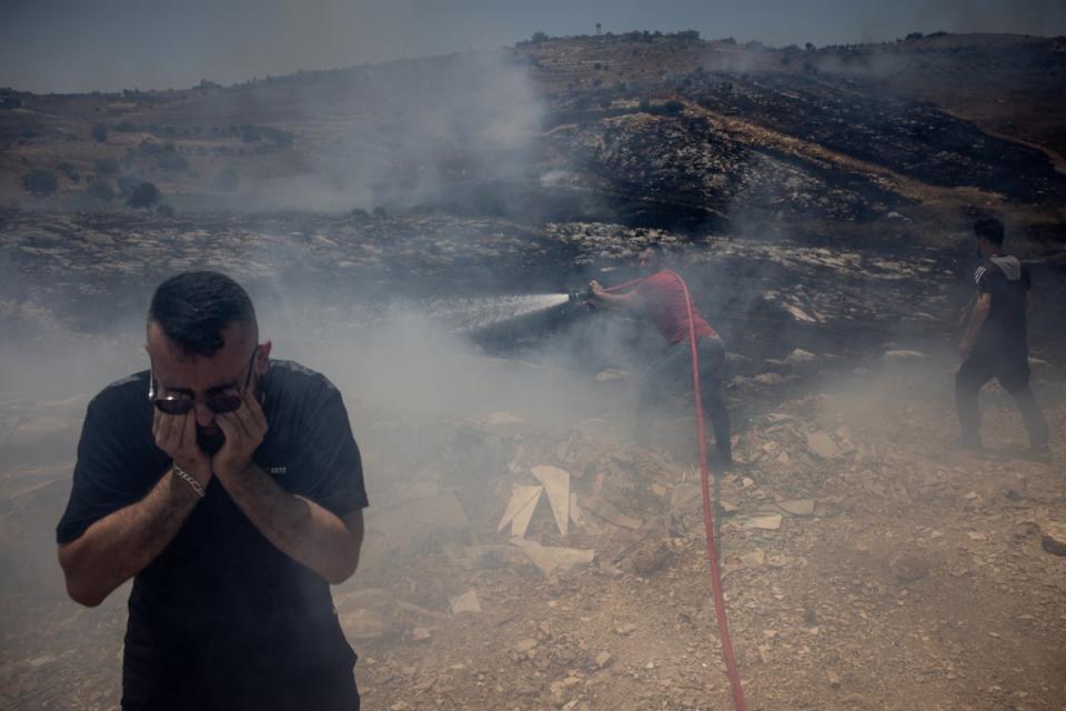 A man protects his eyes from smoke as civilians try to put out fires caused by multiple Israeli strikes that hit targets next to the main road in Bint Jbeil, Lebanon (Getty)