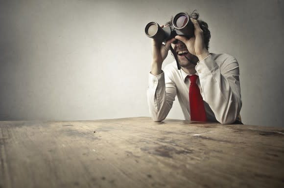 A man in a shirt and tie looking through binoculars.