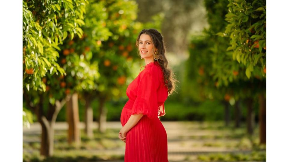 Princess Rajwa standing in an orchard cradling her baby bump