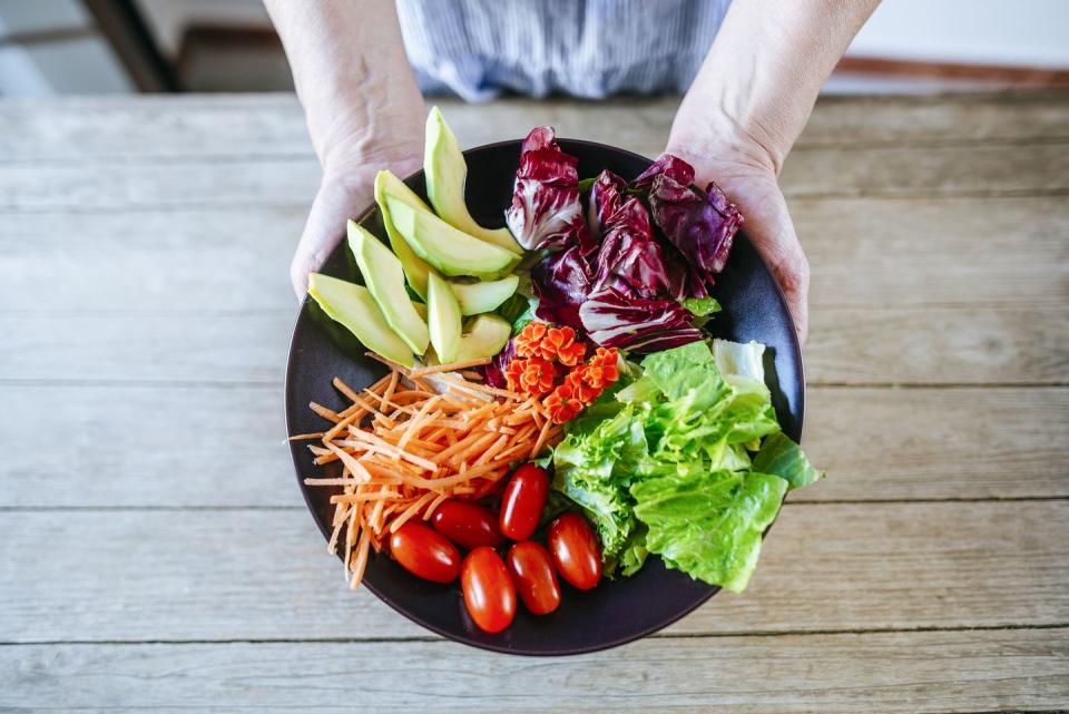 close up salad of avocado, lettuce, tomato and carrot held by woman's hands