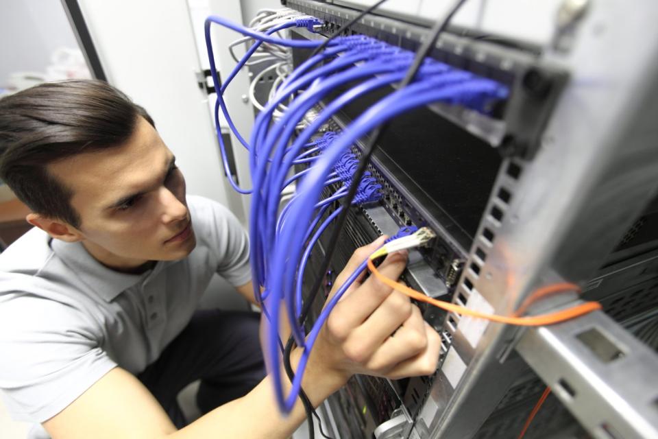 An engineer installs wires in the back of a data center server tower. 