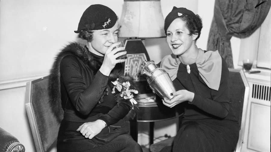 Two women sit and smile as they enjoy a cocktail inside a hotel lounge.