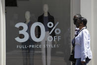 Shoppers walk past a a discount sign at The Grove shopping center Wednesday, May 27, 2020, in Los Angeles. California moved to further relax its coronavirus restrictions and help the battered economy. Retail stores, including those at shopping malls, can open at 50% capacity. (AP Photo/Marcio Jose Sanchez)
